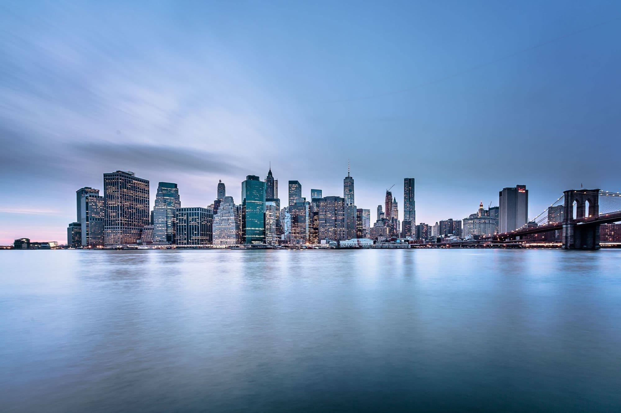 The Manhattan skyline across calm water at dusk.