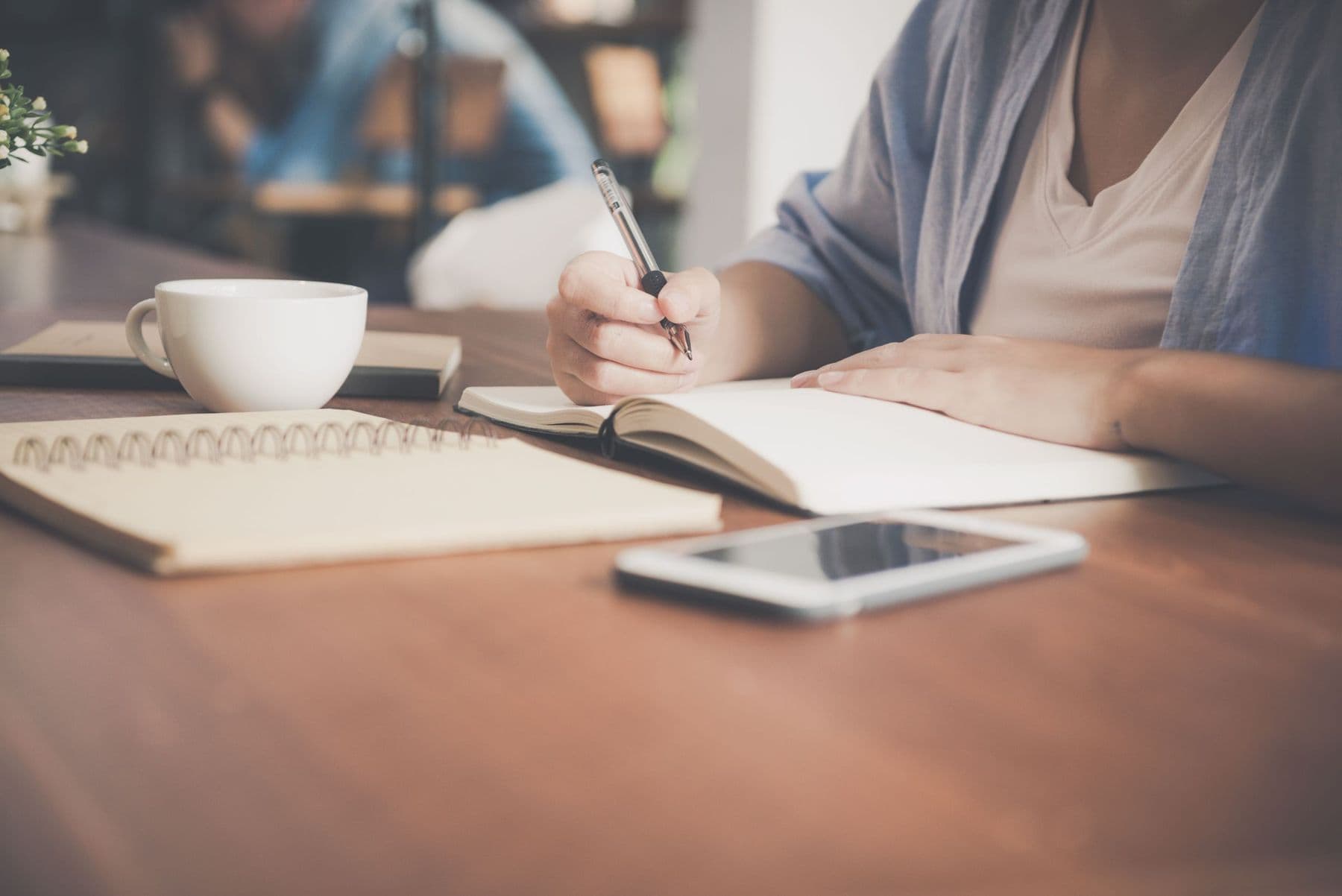 A person writing in a notebook beside a cup of tea.